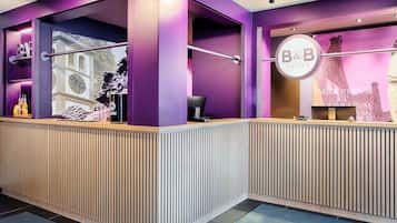 A reception desk with a purple and white color scheme, a large window with a view of a building, and a sign that reads "B&B HOTELS".