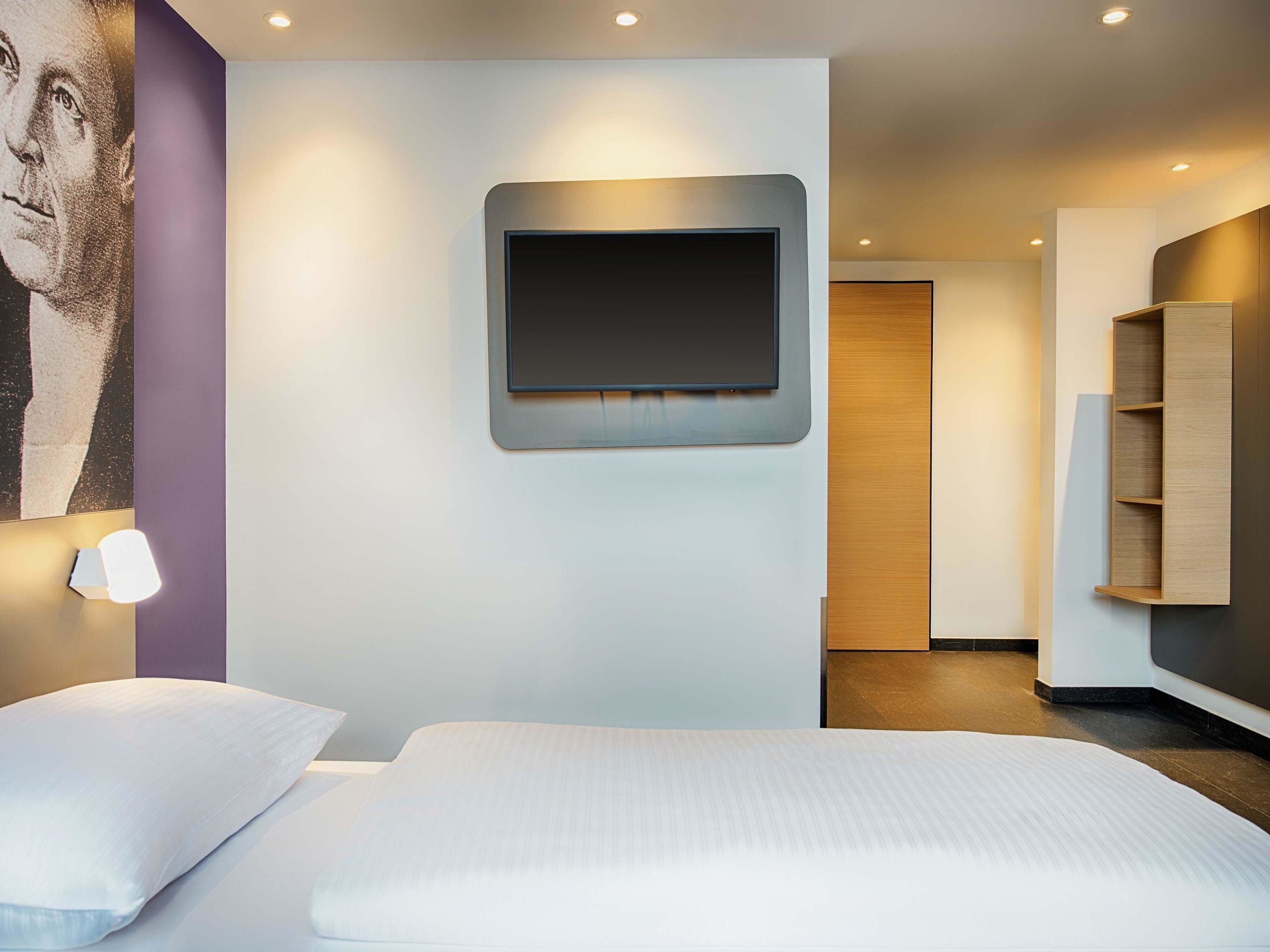 A modern hotel room with a large bed, a mounted TV, and a minimalist design.