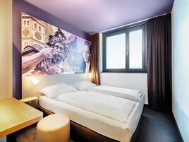 Habitación de hotel con cama, escritorio, silla, ventana con cortinas y un cartel en la pared.