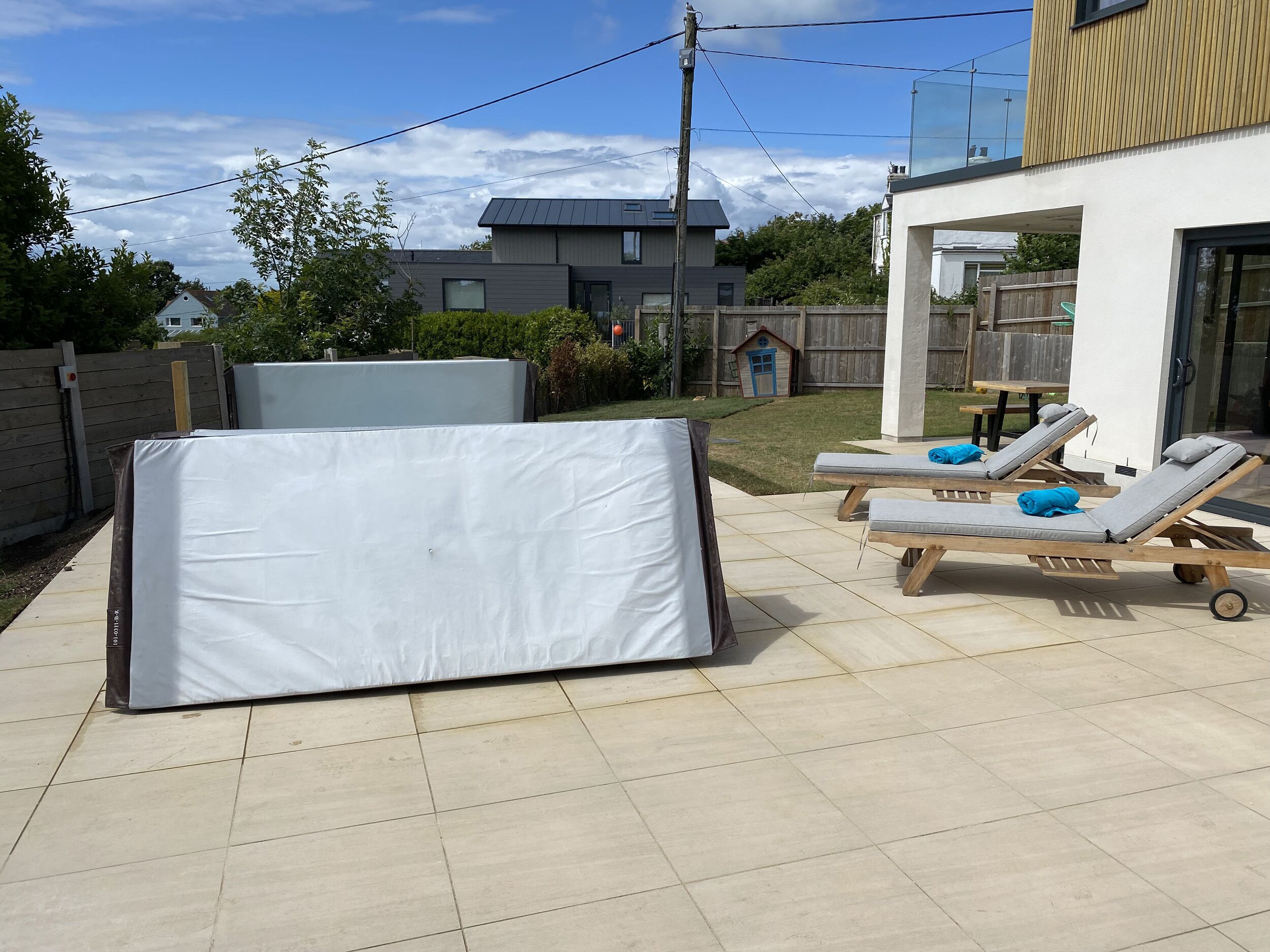 Eine Terrassenfläche mit einer großen Matratze, zwei Lounge-Sesseln mit Kissen und einem Holztisch.