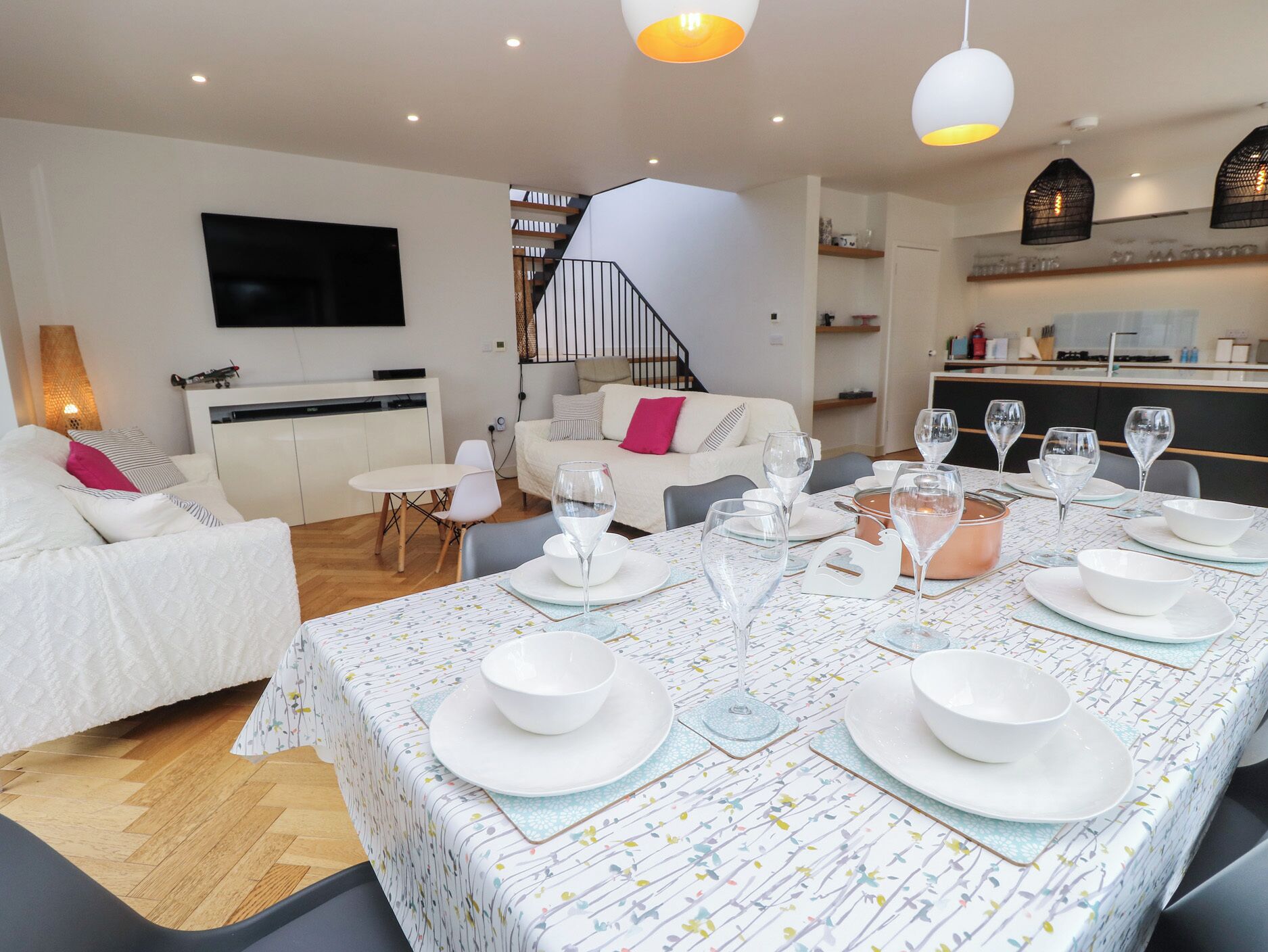 Una sala de estar moderna con comedor listo para una comida, una escalera y una cocina al fondo.