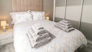 Una cama bien hecha con ropa de cama floral, un cabecero acolchado y dos lámparas de noche.