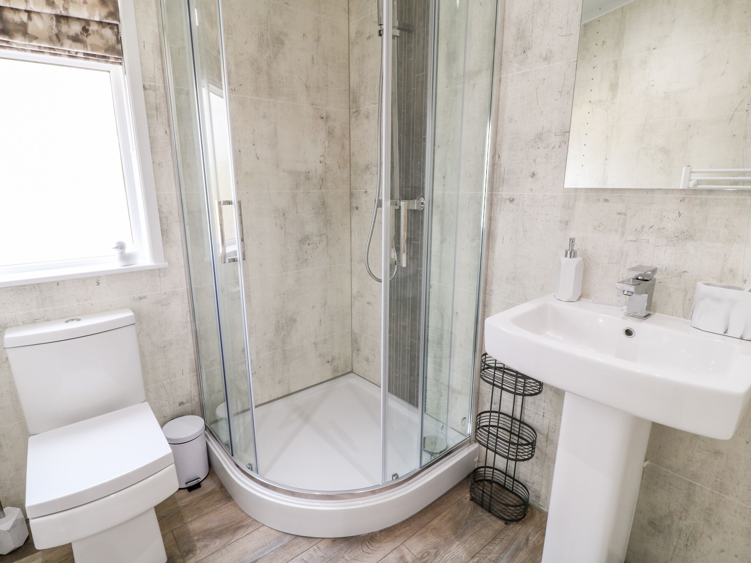 A modern bathroom with a glass-enclosed shower, a white toilet, and a sink with a metal rack.