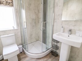 A modern bathroom with a glass-enclosed shower, a white toilet, and a sink with a metal rack.