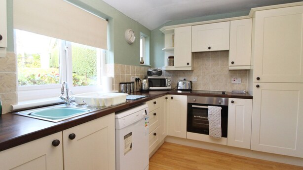 A kitchen with white cabinets, a wooden countertop, a sink, a microwave, a toaster, and a dishwasher. - 2 Mellfell View (Penrith)