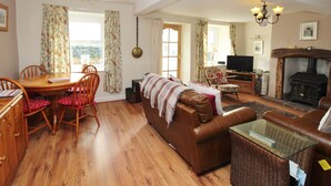 A spacious living room with a fireplace, a dining area with a wooden table and chairs, and a cozy seating area with a leather sofa and a glass coffee table. - 2 Mellfell View (Penrith)
