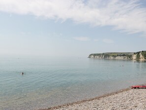 A calm beach with clear water, pebbly shore, and cliffs in the background. - Bay Tree House (Seaton)