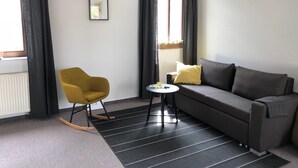 Een moderne woonkamer met een bank, een schommelstoel, een bijzettafeltje en een raam met gordijnen.