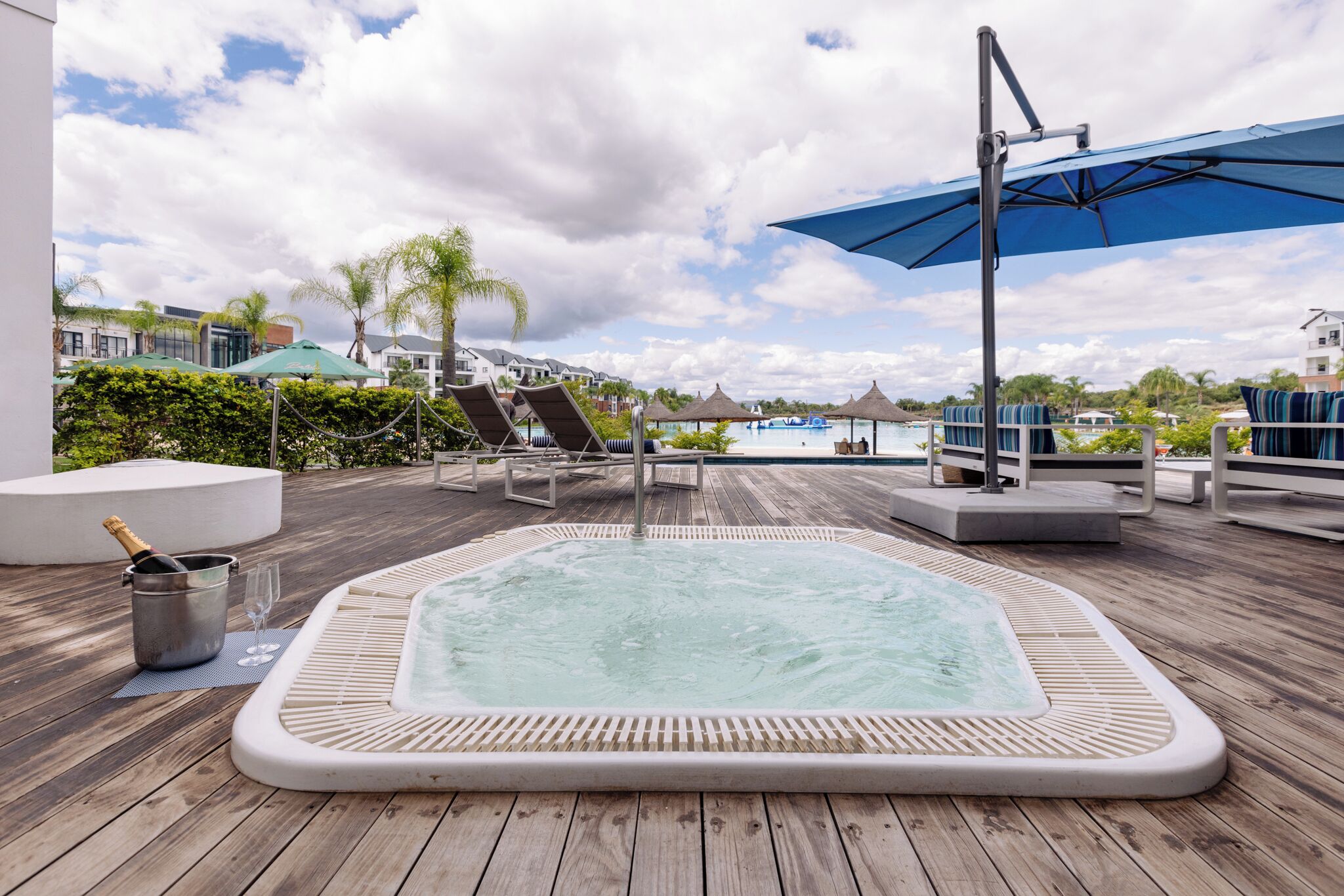 Una terraza de madera con un jacuzzi, sillas de descanso y sombrillas.