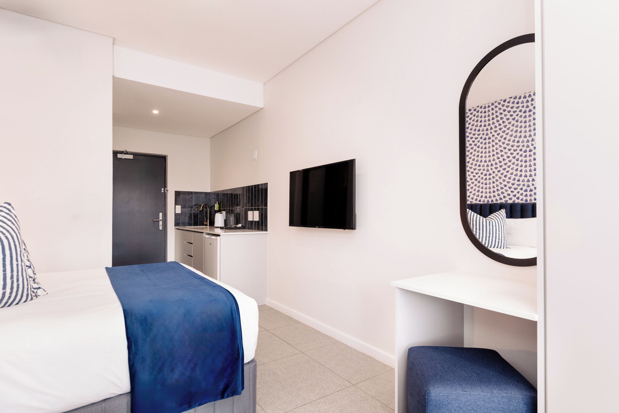 Ein modernes Hotelzimmer mit Bett, Schreibtisch, Spiegel und Fernseher.