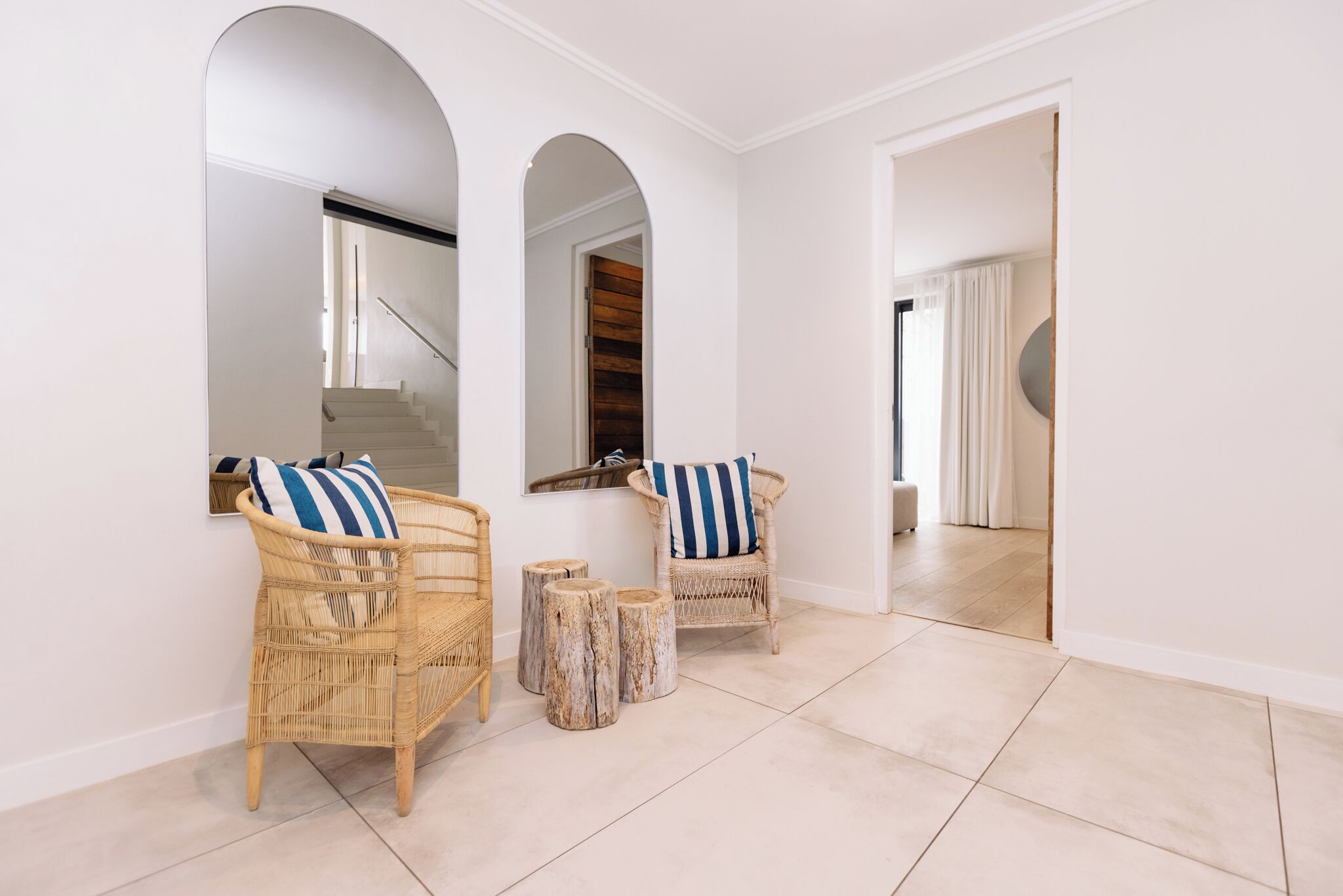 A spacious hallway with white walls, a staircase, and two wicker chairs with striped cushions.