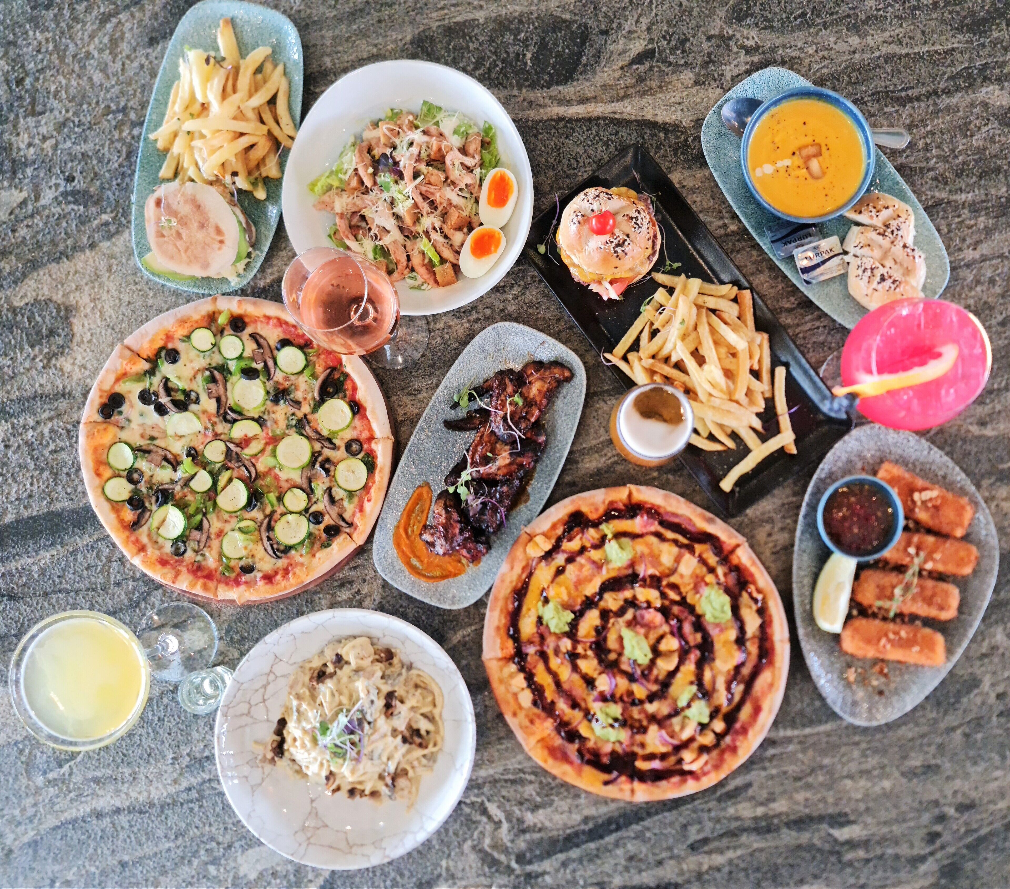 A variety of dishes including pizza, salad, and burgers, arranged on a table.