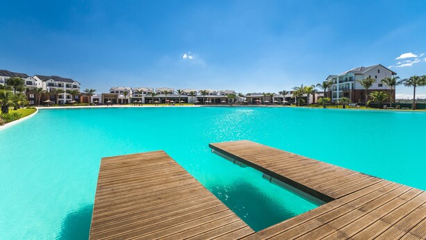 A large, clear blue pool with wooden deck areas, surrounded by modern buildings and palm trees. - MINT Resorts the Blyde (Pretoria)