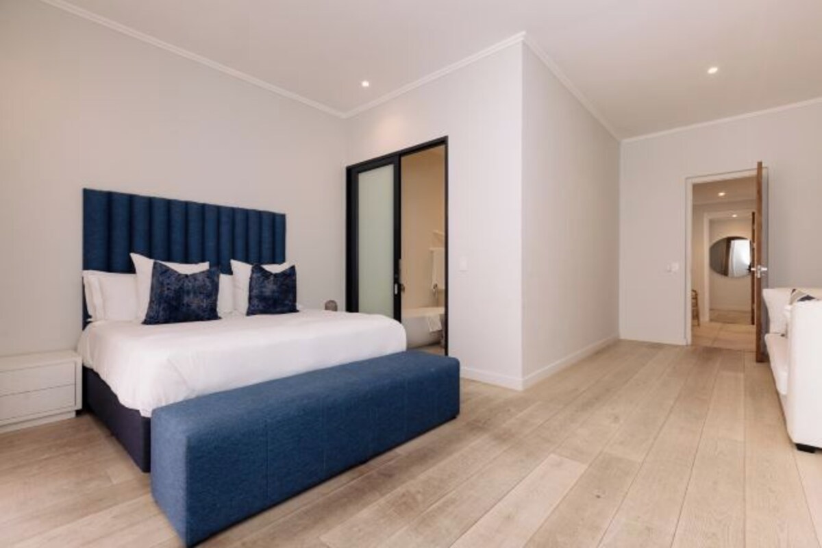 A modern bedroom with a large bed, a bench, and a sliding door leading to a bathroom.