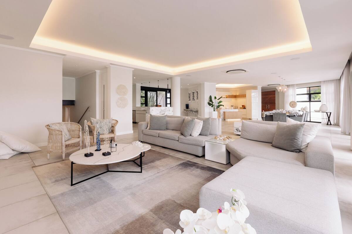 A modern living room with a sofa, armchairs, and a coffee table. There is a kitchen area visible in the background.