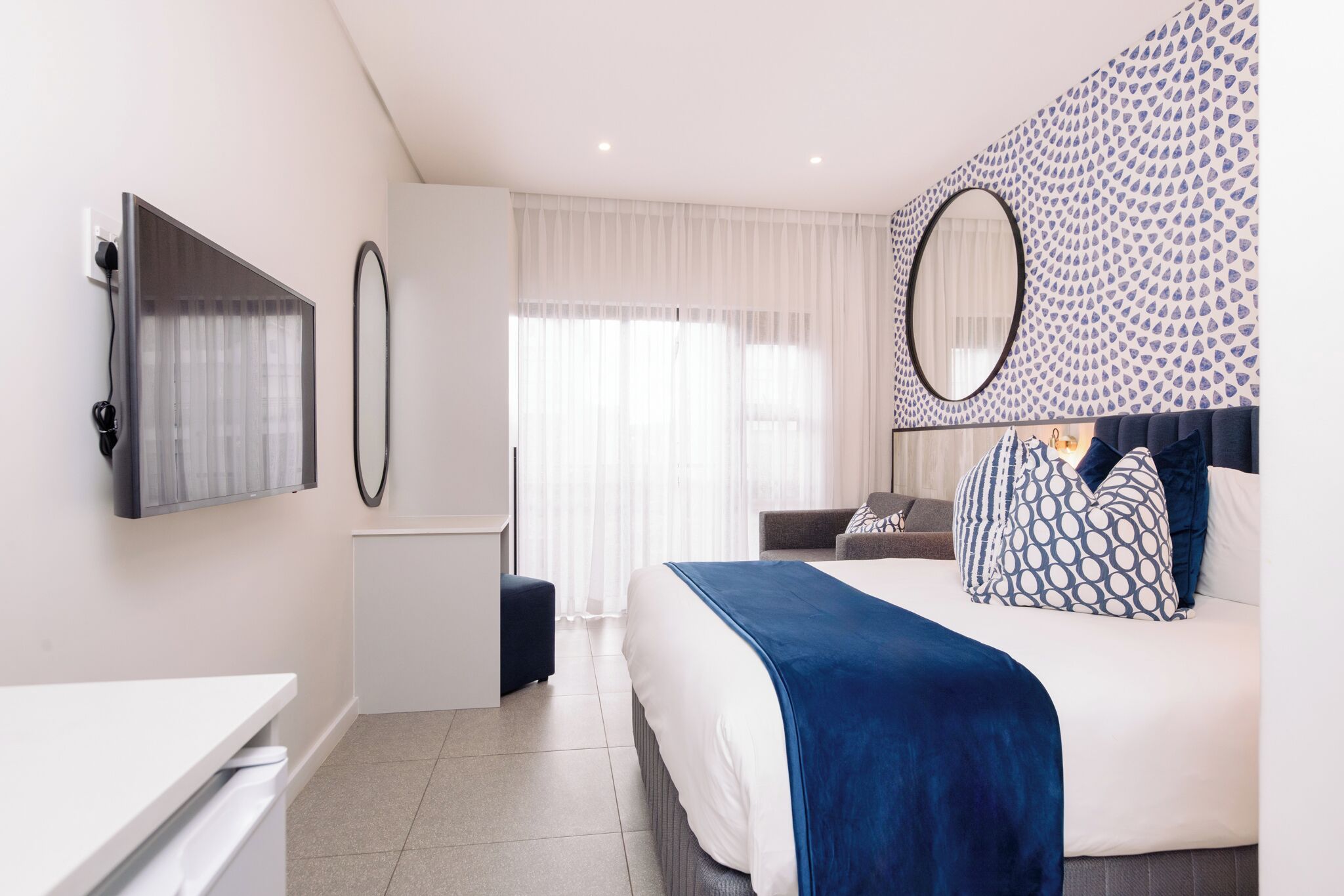 Habitació d'hotel moderna amb llit, escriptori, cadira i un gran mirall.