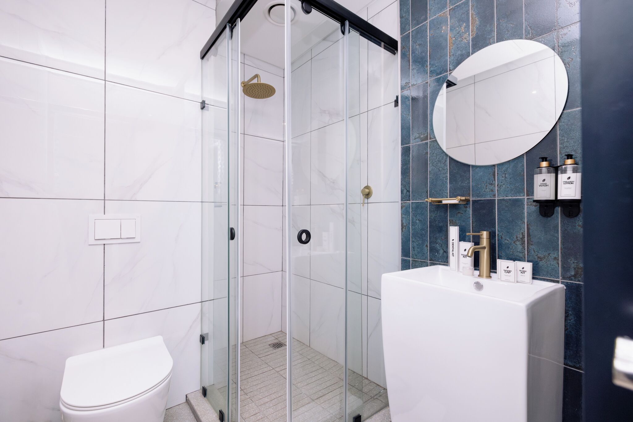 A modern bathroom with a glass-enclosed shower, a white toilet, and a white sink with gold fixtures.