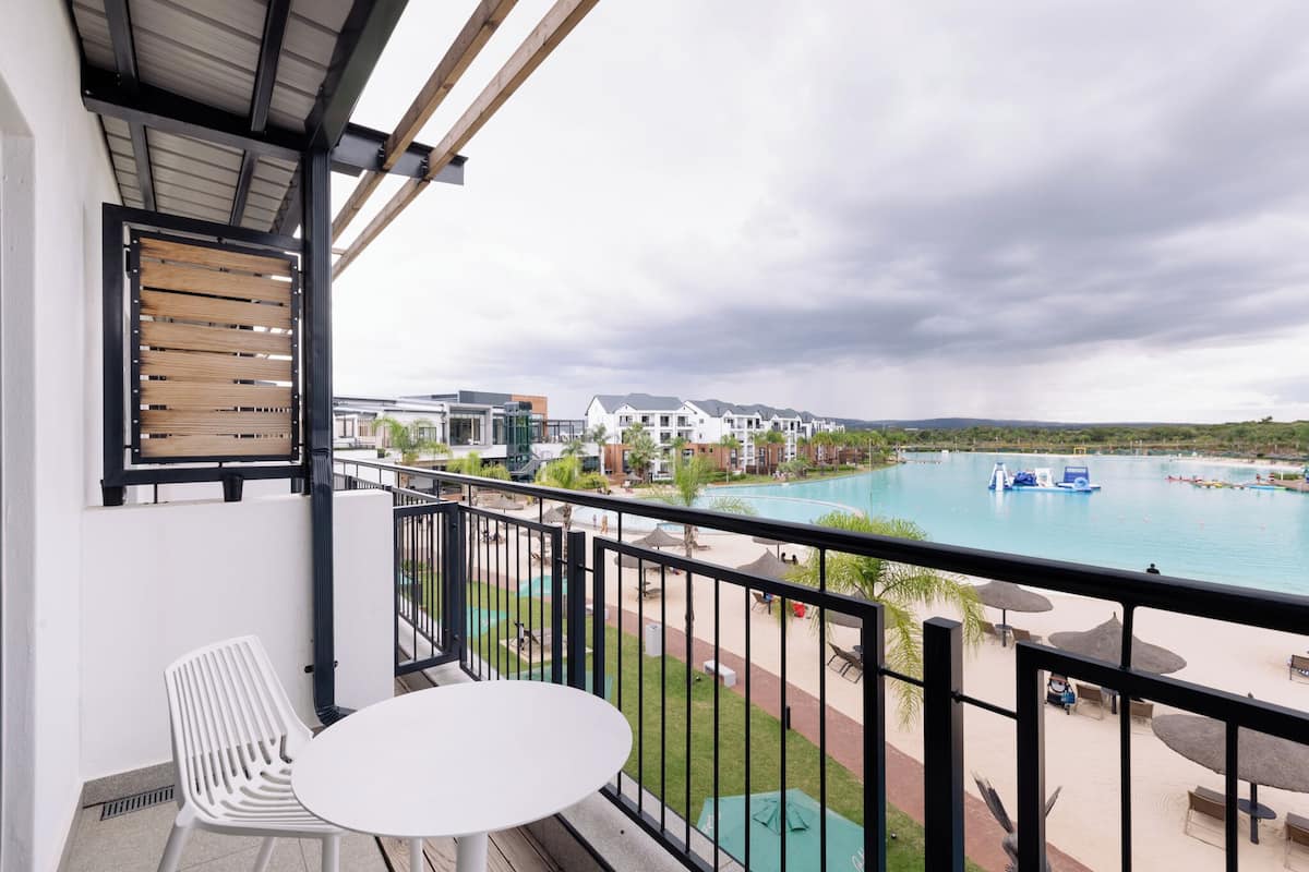 A balcony with a white table and chair, overlooking a swimming pool area with lounge chairs and umbrellas.