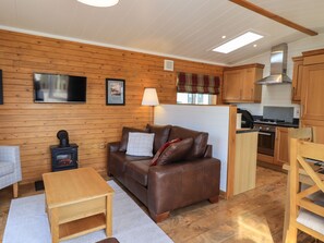 A cozy cabin interior with a wooden interior, a sofa, a small table, a fireplace, and a kitchen area.