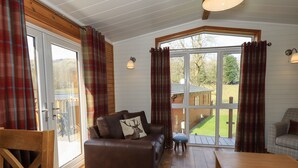 Ein gemütliches Wohnzimmer mit einer braunen Ledersofa, einem Holztisch und Blick auf eine Holzterrasse und einen Außenbereich durch große Fenster.