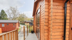 Eine Holzterrasse führt zu einer Hütte mit Glastür, umgeben von weiteren Hütten.