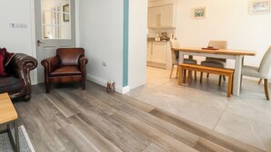 Un salon avec un canapé en cuir marron, une table basse en bois et un coin repas comprenant une table et des chaises en bois.