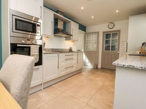 A modern kitchen with white cabinetry, a built-in microwave, a stainless steel range hood, and a granite countertop. - Low Orchard House (Preston)