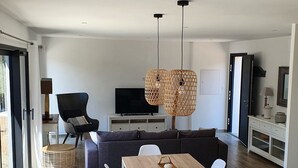 Un salon moderne comprenant un coin repas, un ensemble de canapés, un téléviseur et un espace cuisine.