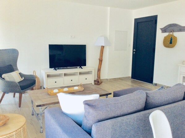 Una sala de estar con un sofá, una silla, un televisor, una lámpara y piso de madera.