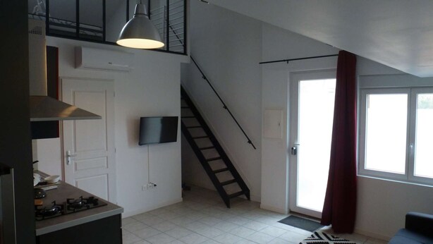 A modern kitchen with a gas stove, a flat-screen TV, and a staircase leading to an upper level. - Le232 fr Meublé 4 Personnes Draps, Serviettes et Ménage Inclus (Chasseneuil-du-Poitou)