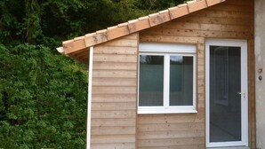 A small wooden cabin with a single window and a door, surrounded by dense greenery. - Le232 fr Meublé 4 Personnes Draps, Serviettes et Ménage Inclus (Chasseneuil-du-Poitou)