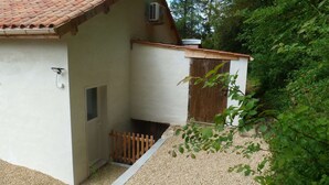 Ein kleines, eingeschossiges Gebäude mit einem Ziegeldach, einer Holztür und einem Kiesweg, der zu einem Holztor führt.