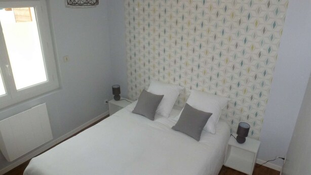 Ein Schlafzimmer mit einem Bett, zwei Nachttischen, einem Fenster und einem gemusterten Kopfteil.