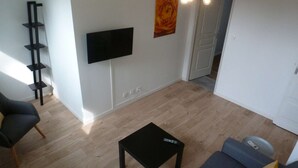 Ein Zimmer mit einem an der Wand montierten Flachbildfernseher, einem schwarzen Tisch, einem grauen Sofa und einem Holzboden.