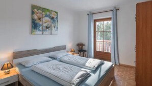 Ein Schlafzimmer mit zwei Betten, einem Nachttisch, einer Lampe, einem Fenster mit Vorhängen und einer Holztür.