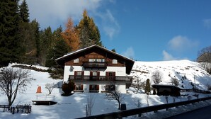 Ein Chalet mit Balkon, umgeben von schneebedeckten Bäumen und blauem Himmel.