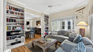 A spacious living room with a large bookshelf, a comfortable sofa set, and a dining area. - Modern Grand Pavillon Home: Steps to Beach, Pool Access (Isle Of Palms)