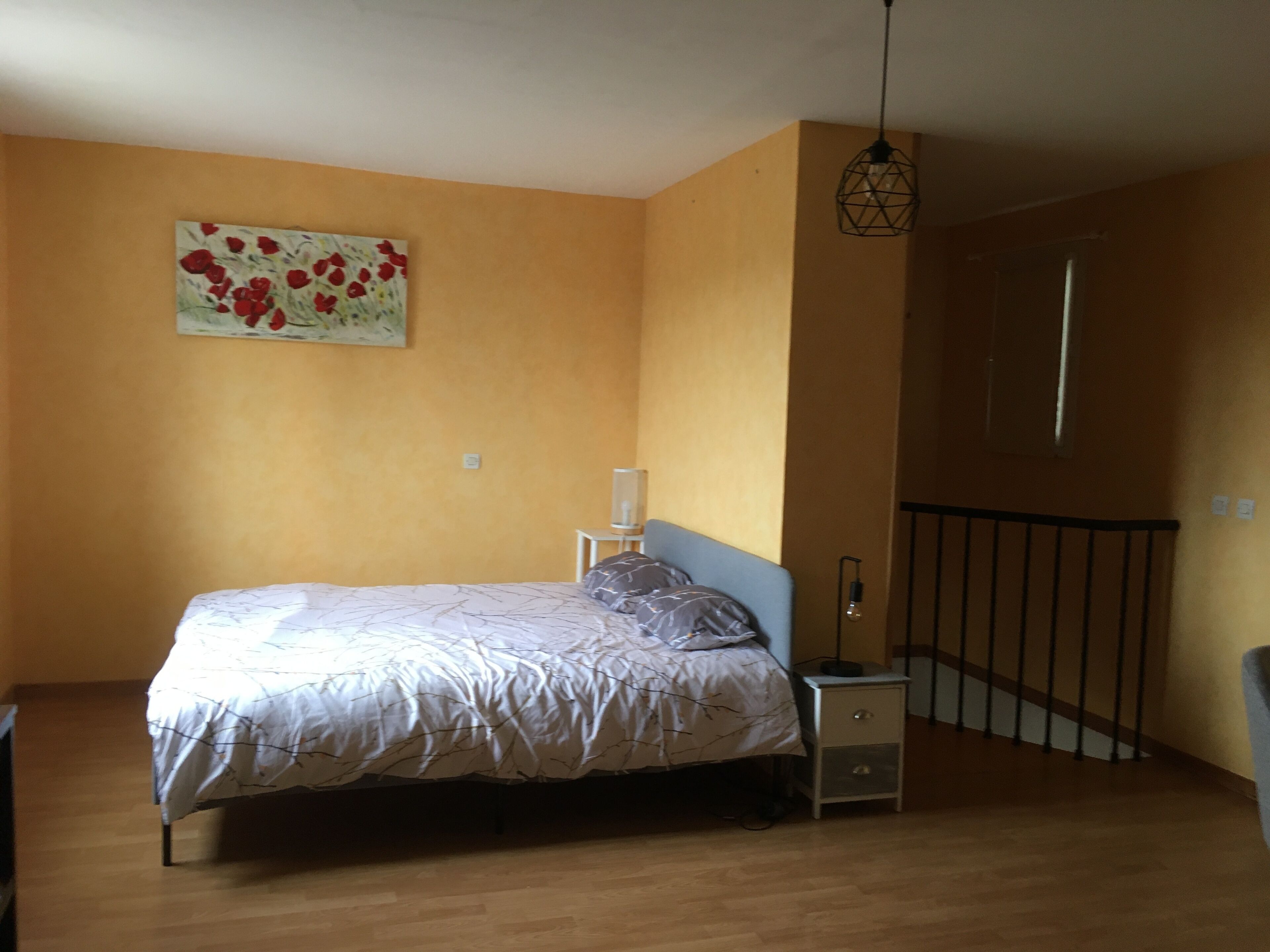Un dormitorio con cama, mesita de noche, lámpara, un cuadro en la pared y una escalera.