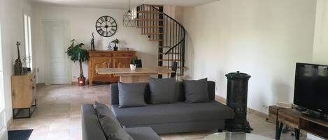 Una sala de estar moderna con un sofá, una mesa de centro de vidrio, un televisor y una escalera que sube a un nivel superior.