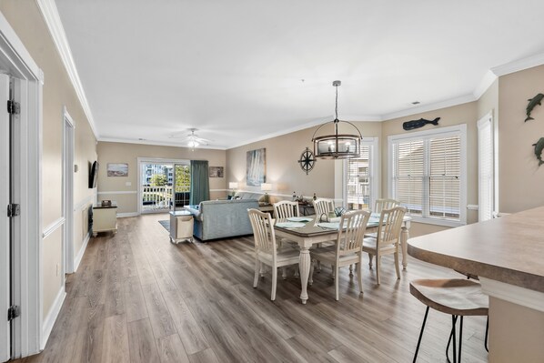 A spacious kitchen with a dining area, wooden flooring, and a view to the outside.