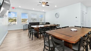 A modern meeting room with a wooden table, black chairs, a ceiling fan, and a clock on the wall.