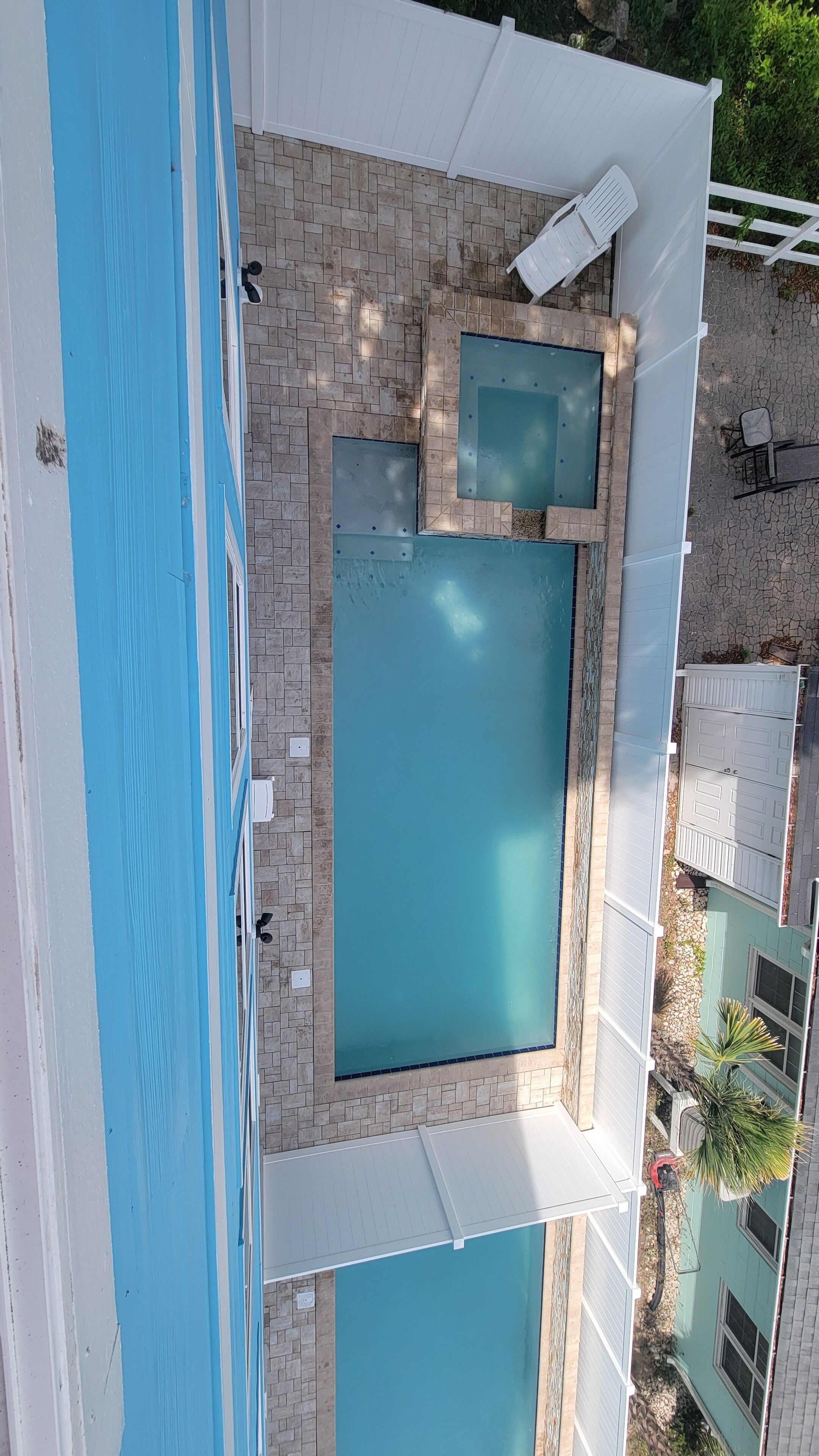 Una piscina en la azotea con dos áreas separadas, rodeada por una cerca blanca y un patio de ladrillo.