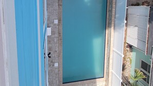 A rooftop pool with two separate sections, surrounded by a white fence and a brick patio.