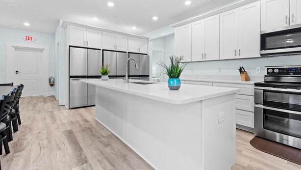 A modern kitchen with white cabinetry, stainless steel appliances, and a central island with a blue vase.