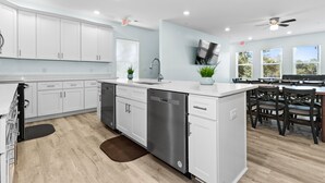 A modern kitchen with white cabinets, a dishwasher, a sink, and a dining area with chairs and a table.