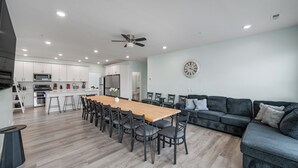 A modern kitchen with white cabinets, a wooden dining table, and a black sofa.