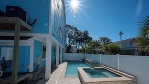 A swimming pool area with a wooden deck, a white fence, and a blue building in the background.