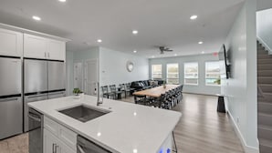 A modern kitchen with stainless steel appliances, a central island, and a dining area with a long table and chairs.