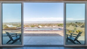 A room with a large sliding glass door leading to an outdoor area with a pool, lounge chairs, and a view of distant mountains.
