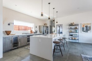 A modern kitchen with a central island, stainless steel appliances, pendant lighting, and a large window.